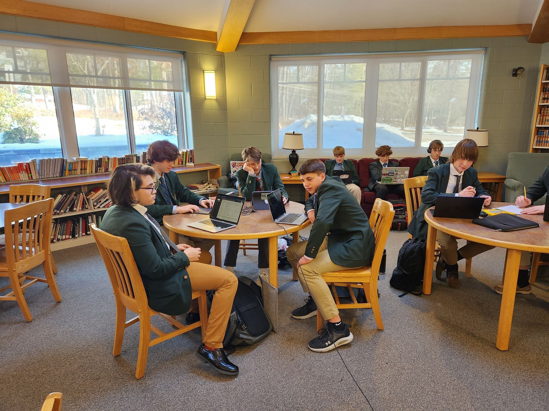 students in the library, sitting at round tables, books and windows