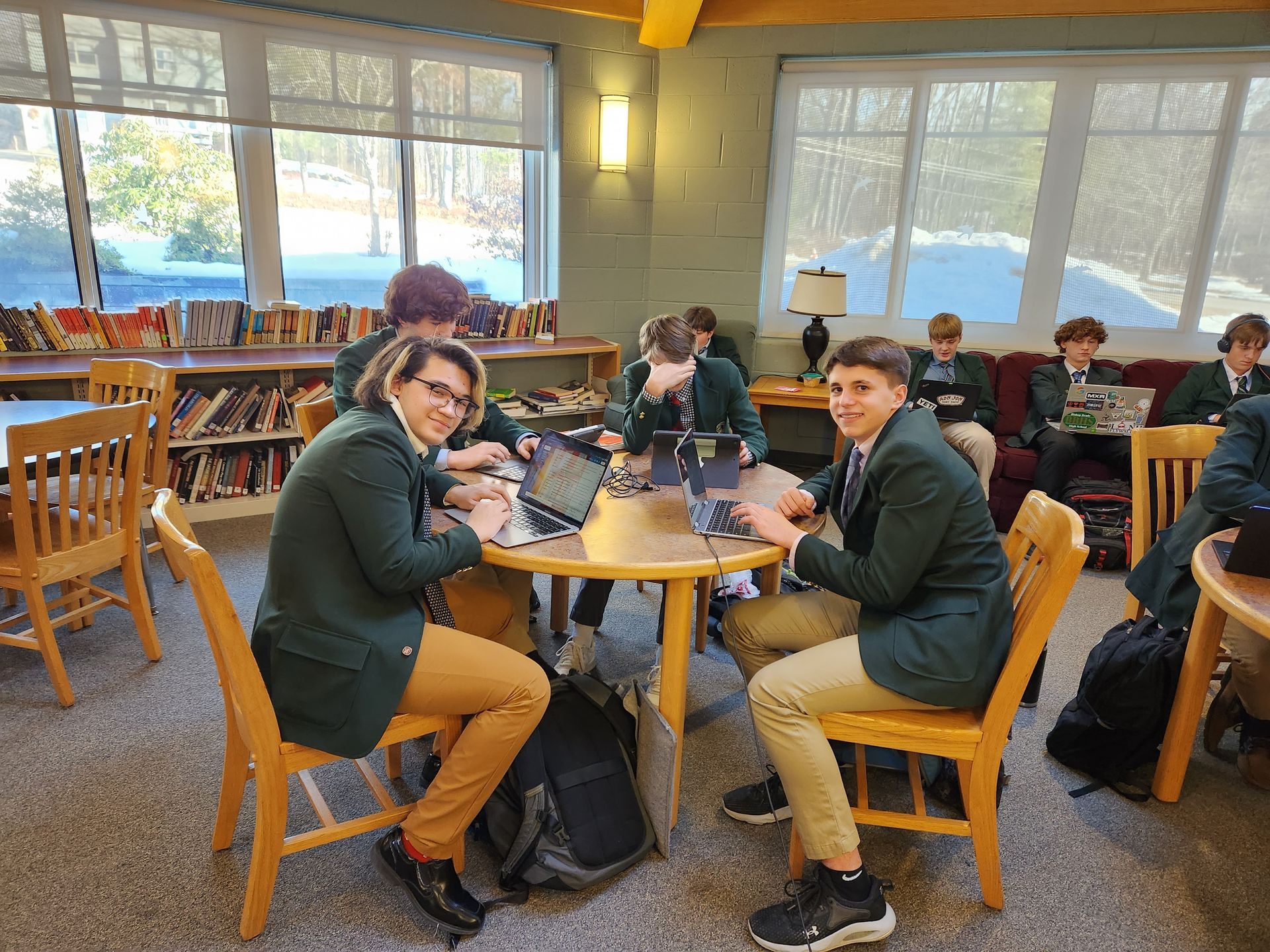 group of students sitting at a round table in the library with windows and book shelf 