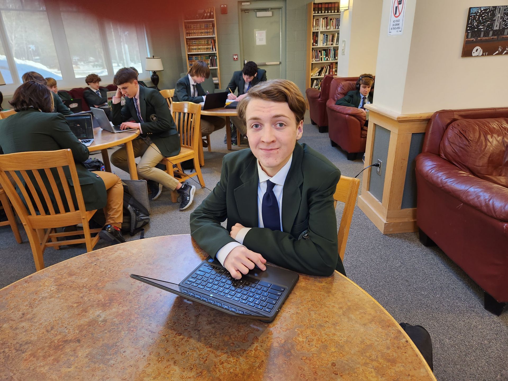 single student smiling at a round table in the library with other students sitting at tables in background