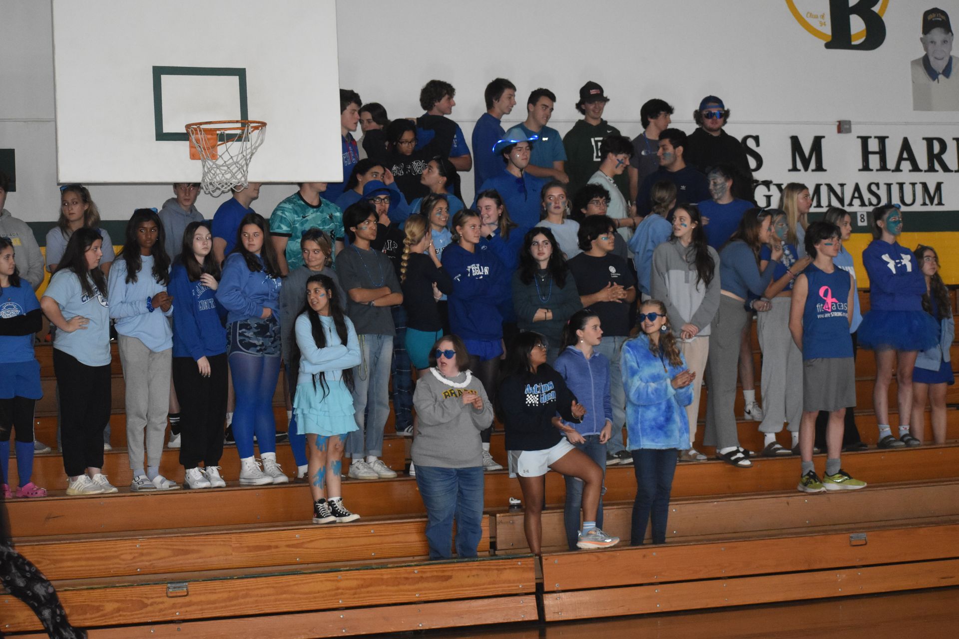 group of students wearing blue standing on high school bleachers in the gym