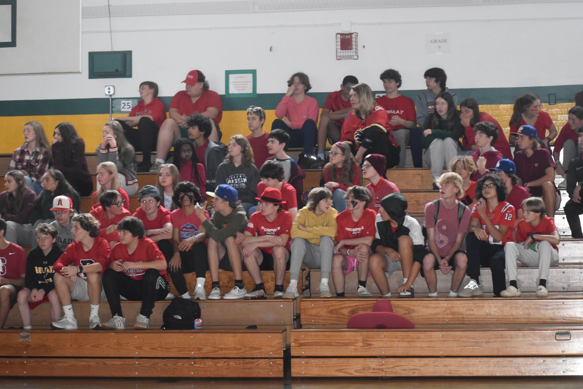 group of students sitting on the bleachers in the gym wearing a lot of red clothing