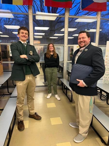 2 students and 1 staff member smiling in the school cafeteria.