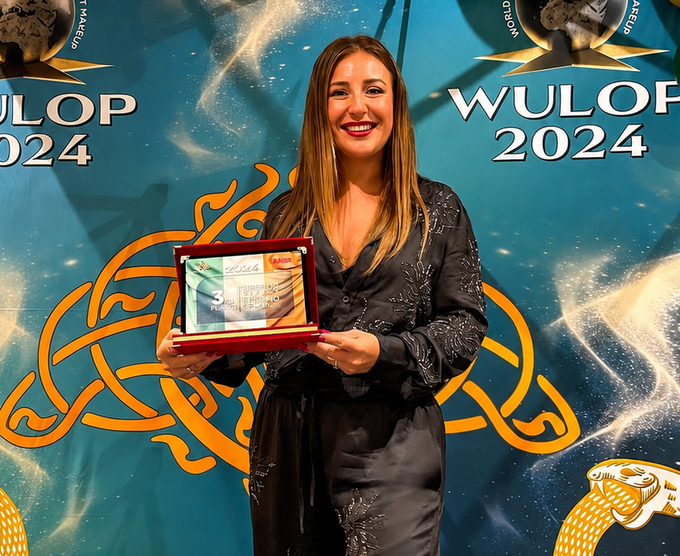 Una donna regge una targa di riconoscimento davanti a uno sfondo blu con la scritta WULOP 2024.