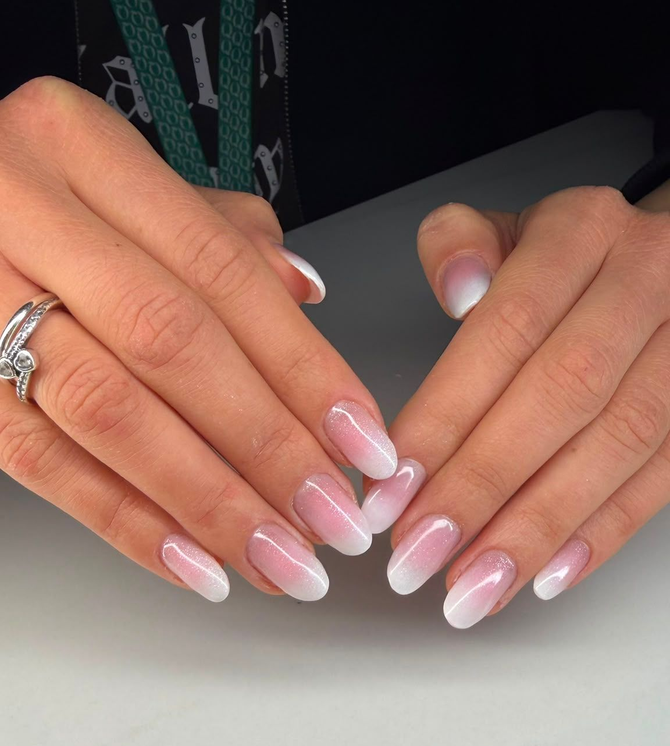 Mani con manicure francese rosa e anello d'argento appoggiate su un tavolo chiaro.