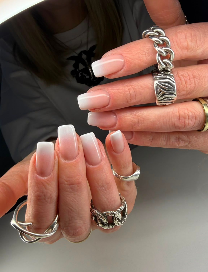 Mani con una lunga manicure francese, adornate da anelli d'argento e bracciali a catena.
