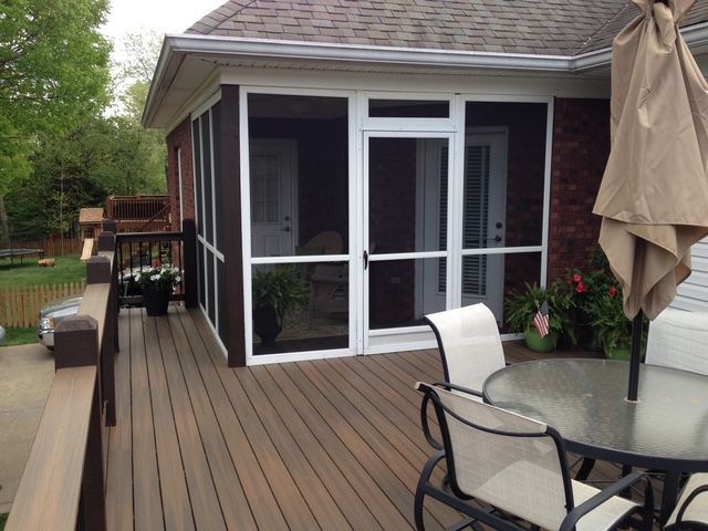 A deck with a table and chairs next to a screened-in porch attached to a house with a brick exterior.