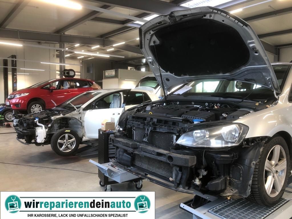 Zwei Autos in einer Autowerkstatt mit geöffneten Motorhauben und abmontierten vorderen Stoßstangen.