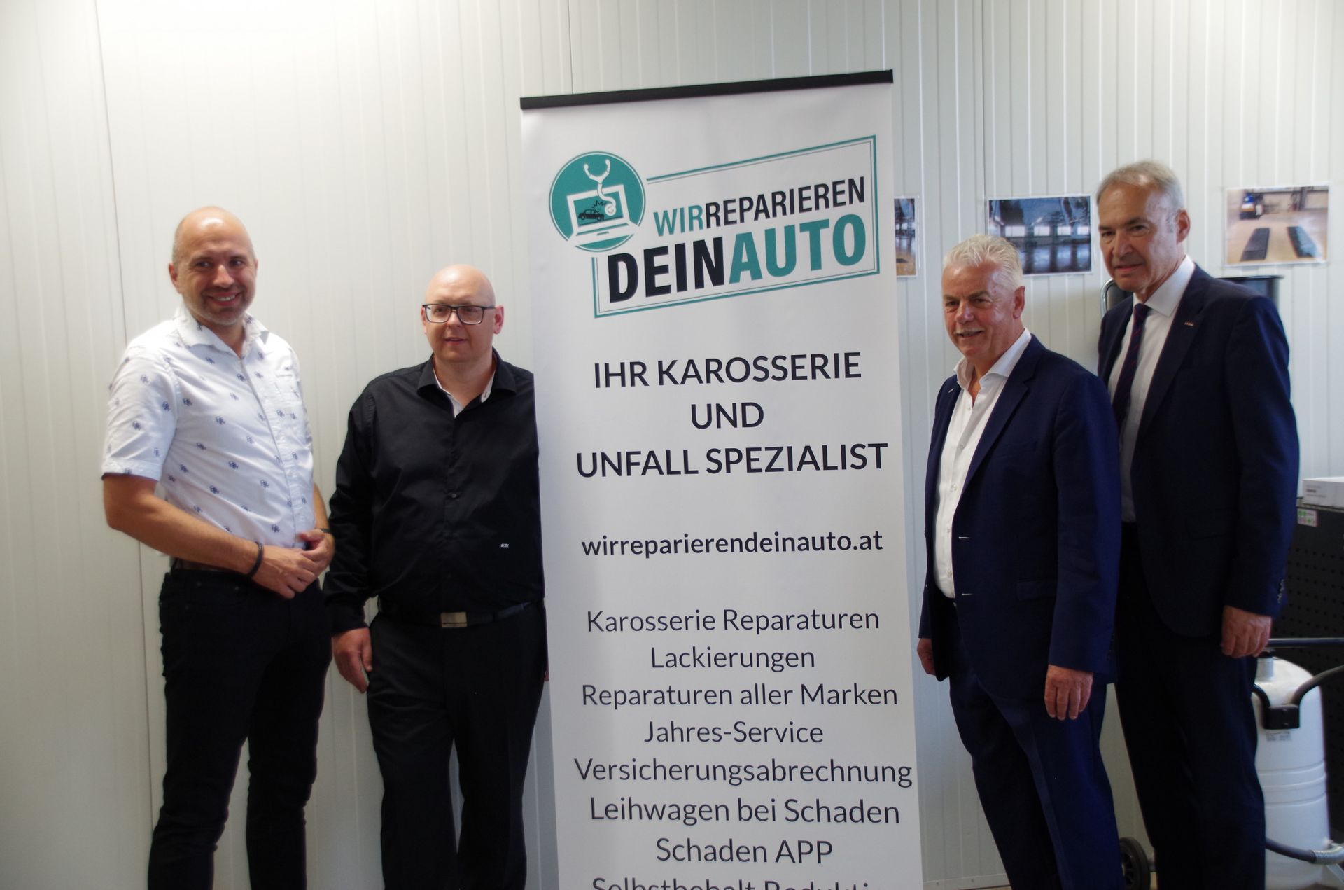 Vier Männer stehen neben einem deutschen Banner bei einer Indoor-Veranstaltung.