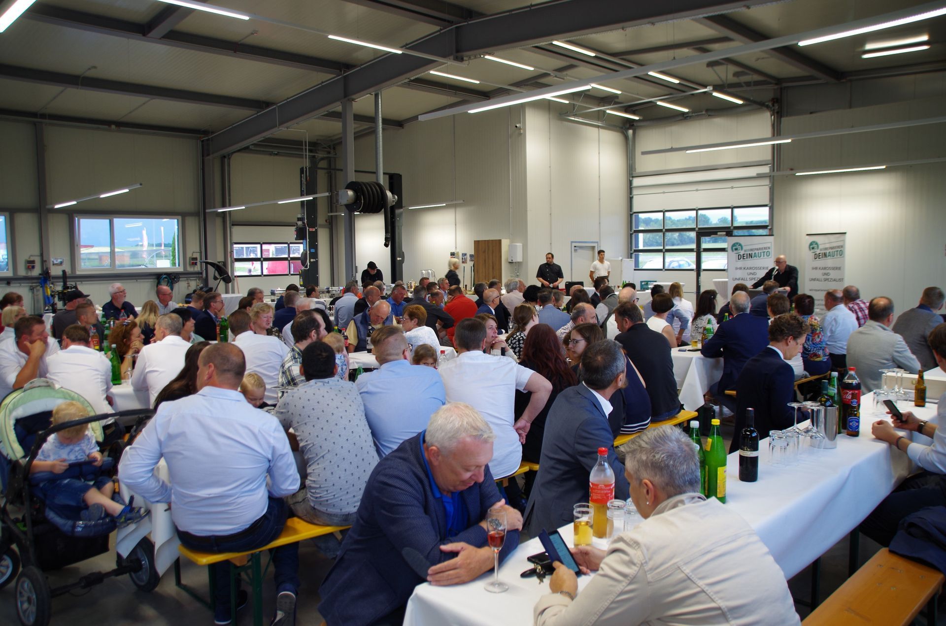 Eine überfüllte Cafeteria, in der Menschen an langen Tischen unter hellem Industrielicht essen und sich unterhalten.