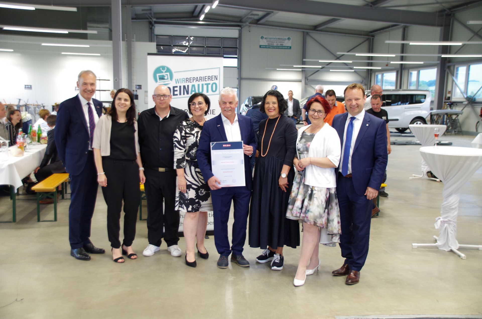 Eine Gruppe von Menschen posiert bei einer Veranstaltung in einer hellen Industriehalle und hält ein Zertifikat in die Höhe.