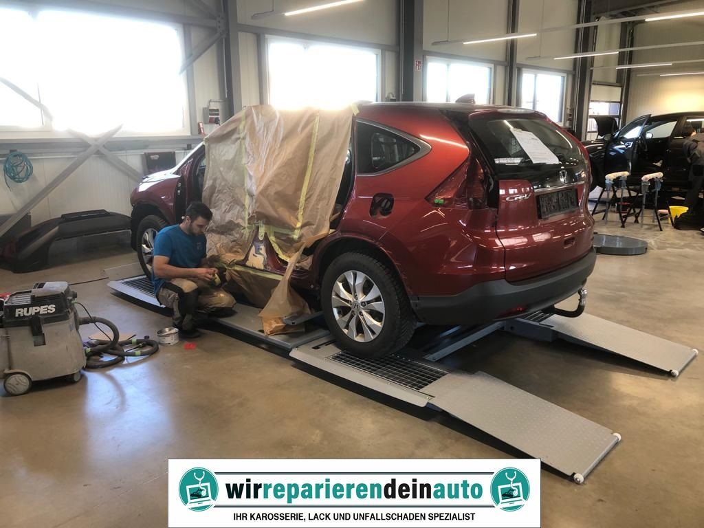 Ein roter SUV steht in der Autowerkstatt auf Rampen, ein Mechaniker arbeitet