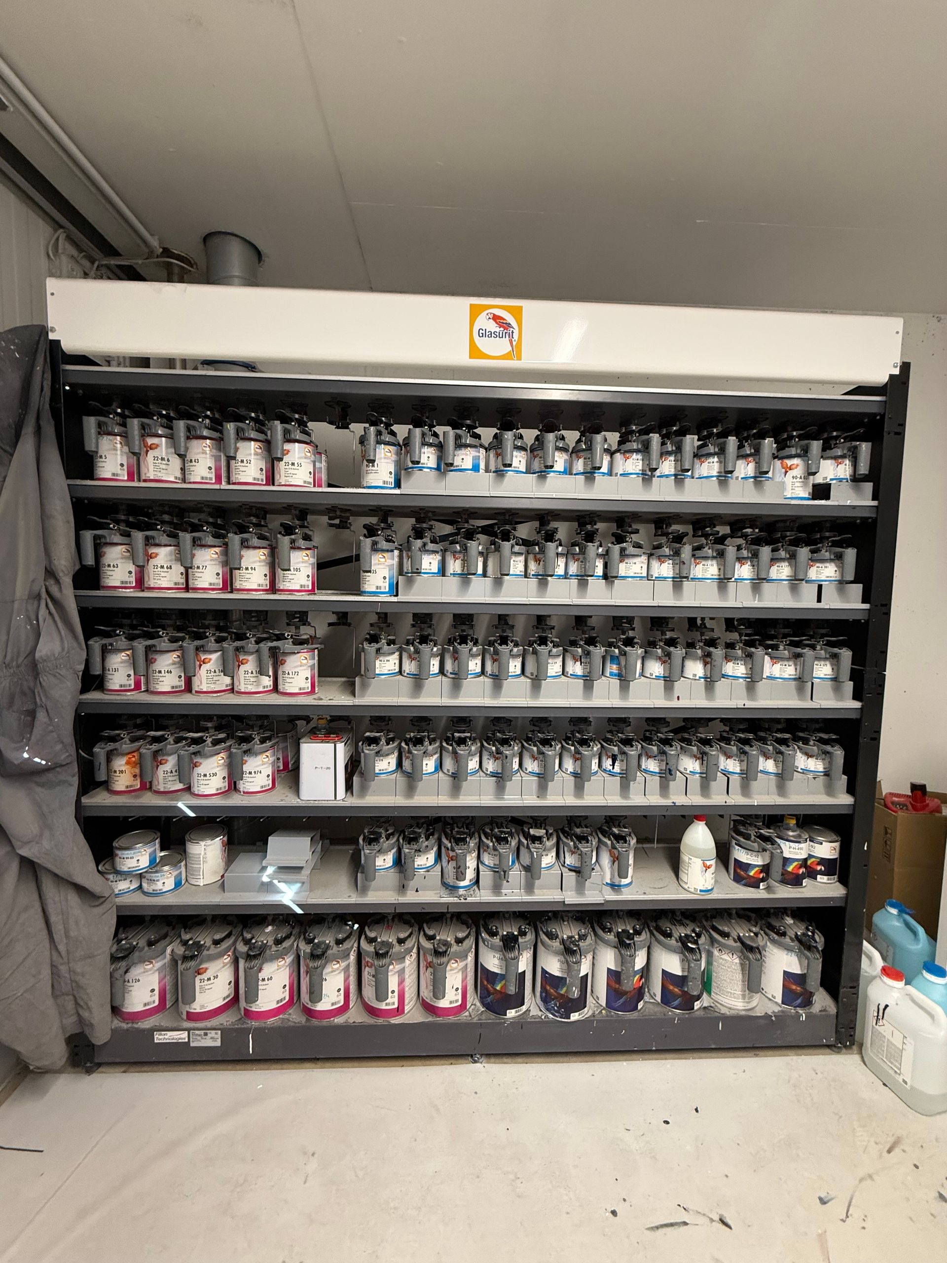 Eine Wand aus Farbdosen auf Metallregalen in einem Hauswirtschaftsraum mit weiß-grauen Wänden.