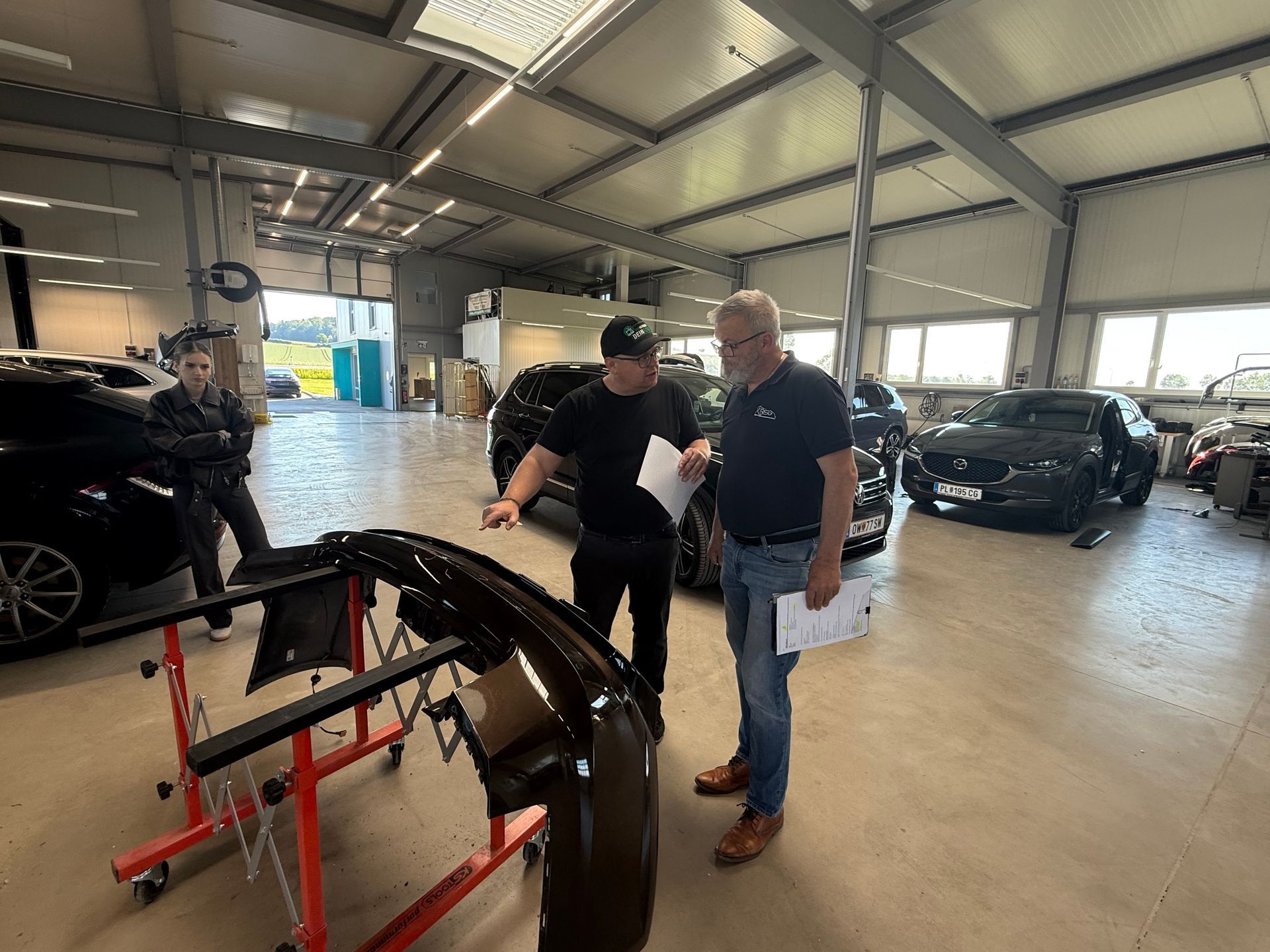 Zwei Männer begutachten eine Autostoßstange in einer hell erleuchteten Autowerkstatt.
