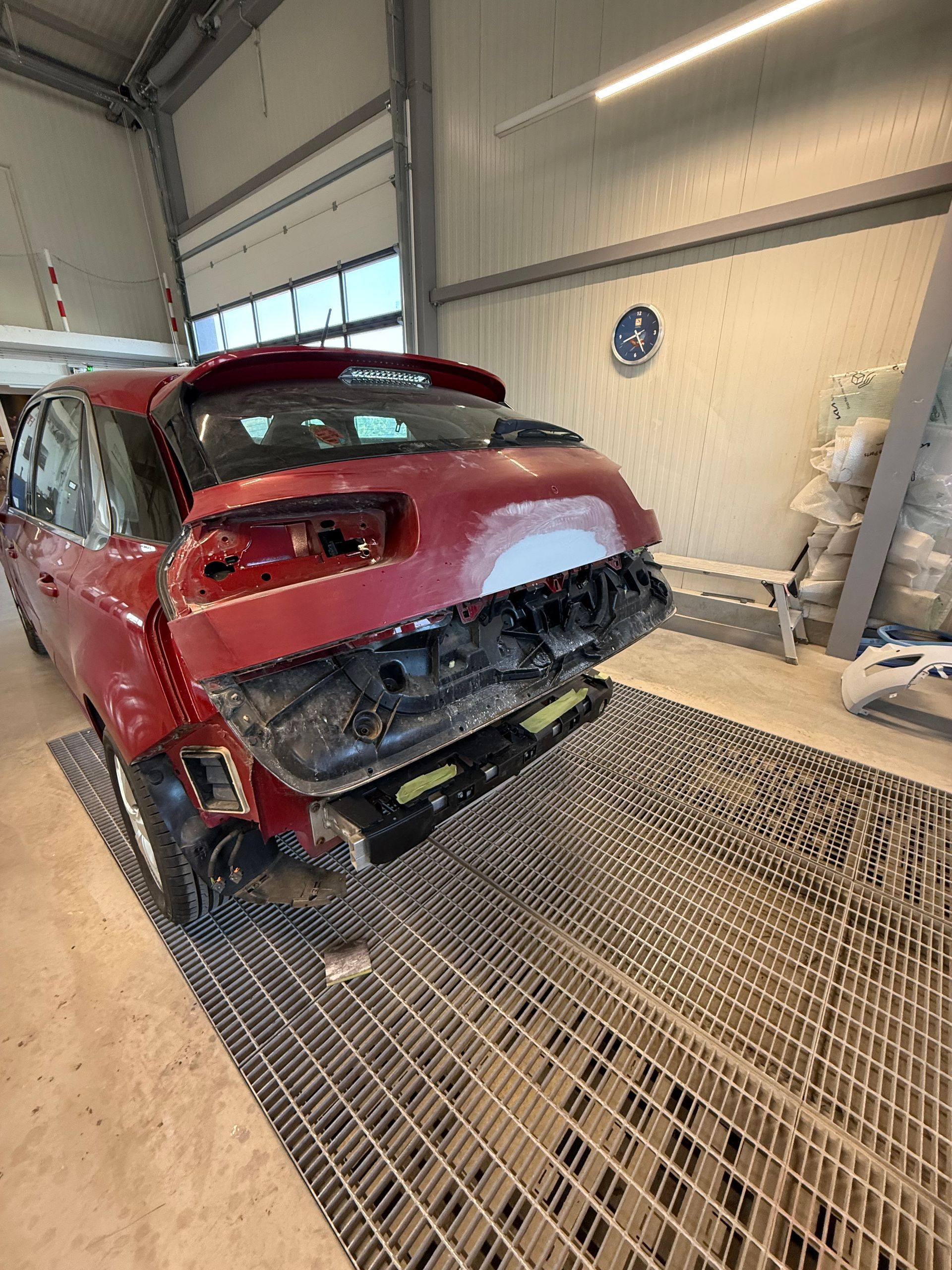 Rotes Auto mit Heckschaden in einer Autowerkstatt, von hinten gesehen.