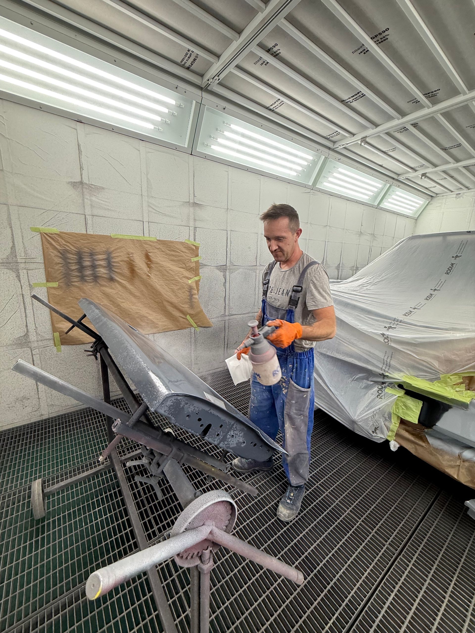 Ein Mann besprüht in einer Werkstatt einen schwarzen Fahrradrahmen mit Sprühfarbe