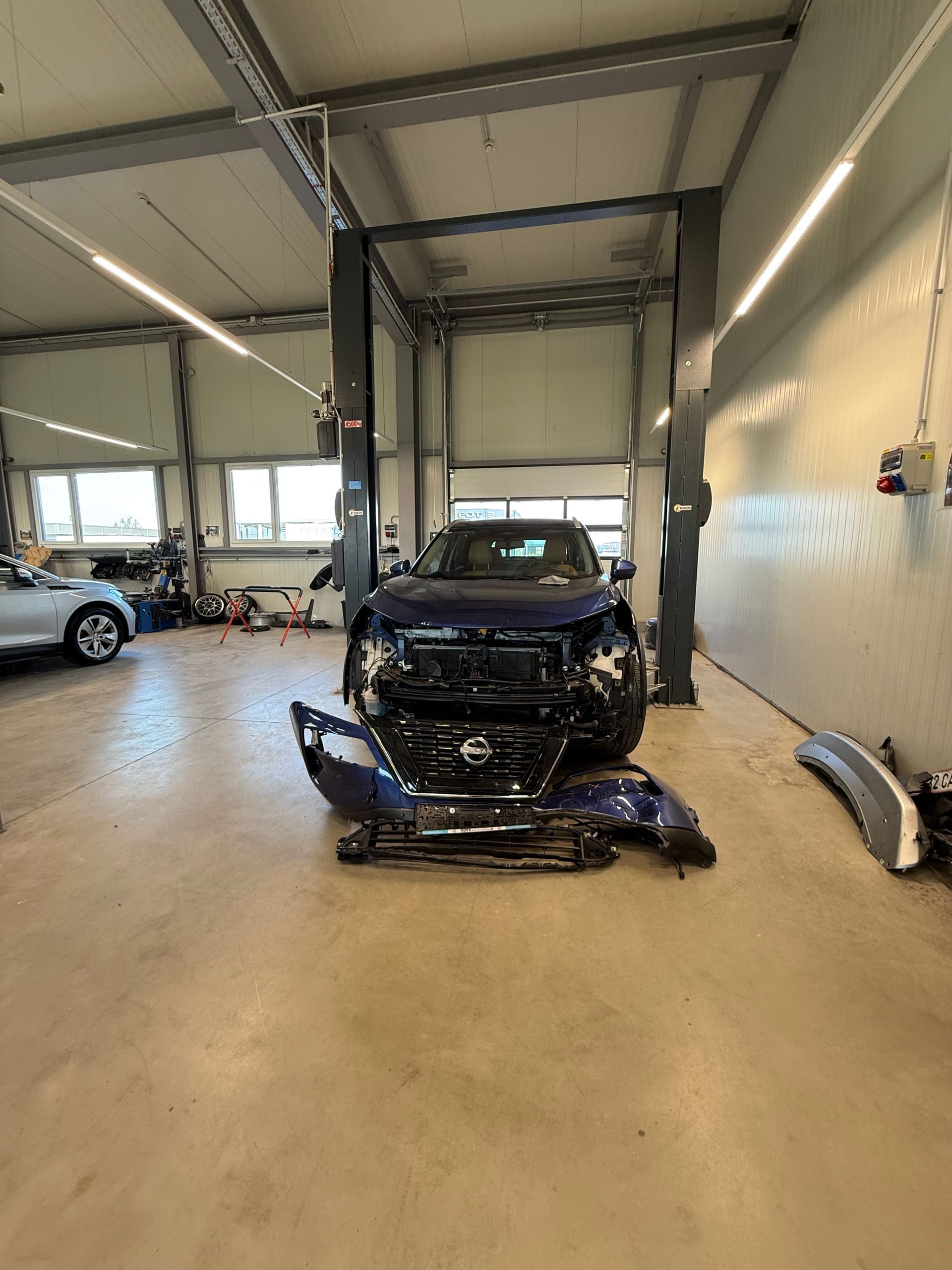 Beschädigter schwarzer Pkw in einer Autowerkstatt, Frontpartie abmontiert, dahinter eine Hebebühne.