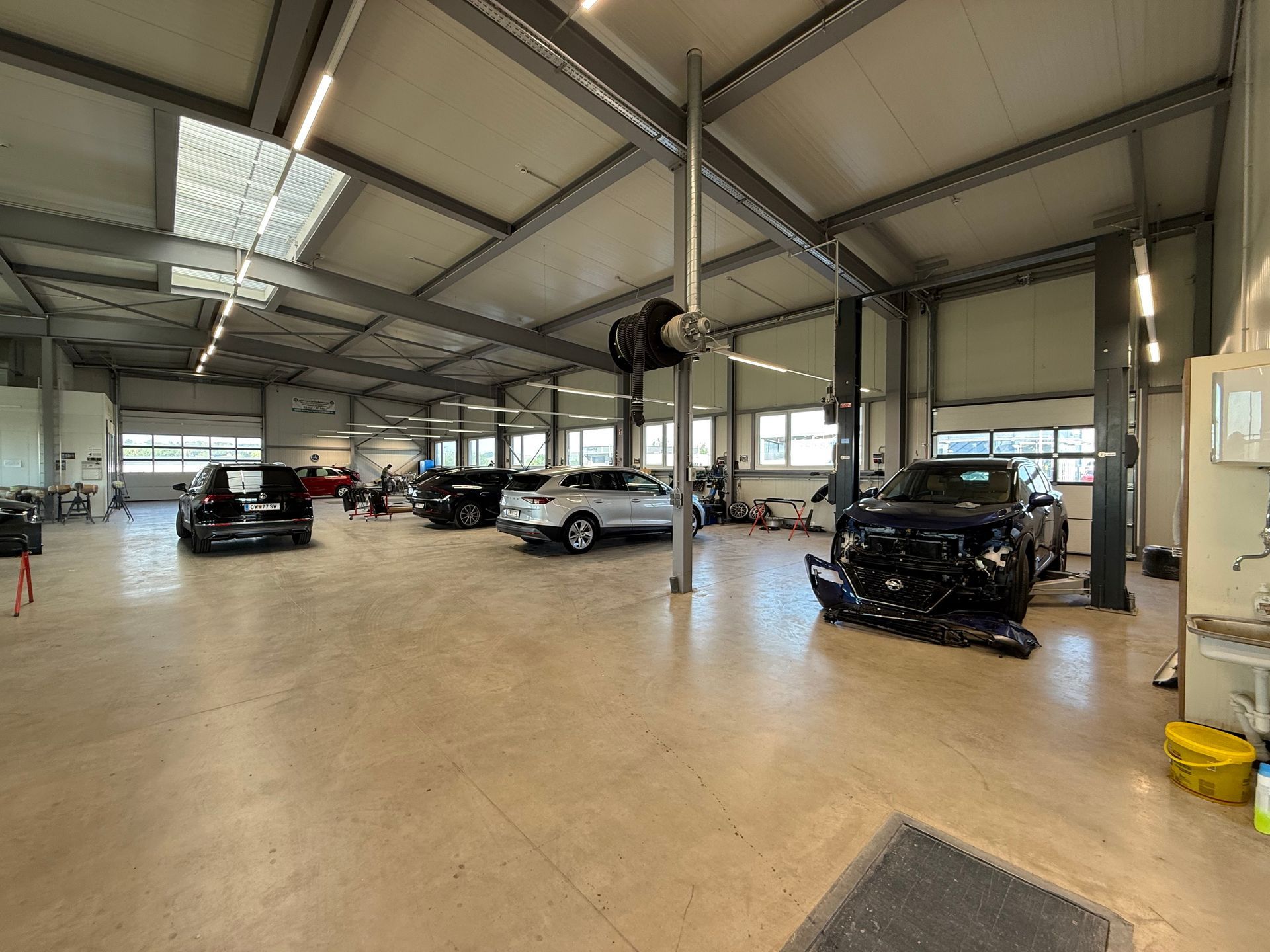 Großer überdachter Autohaus-Showroom mit mehreren geparkten Fahrzeugen unter einem hohen Metalldach