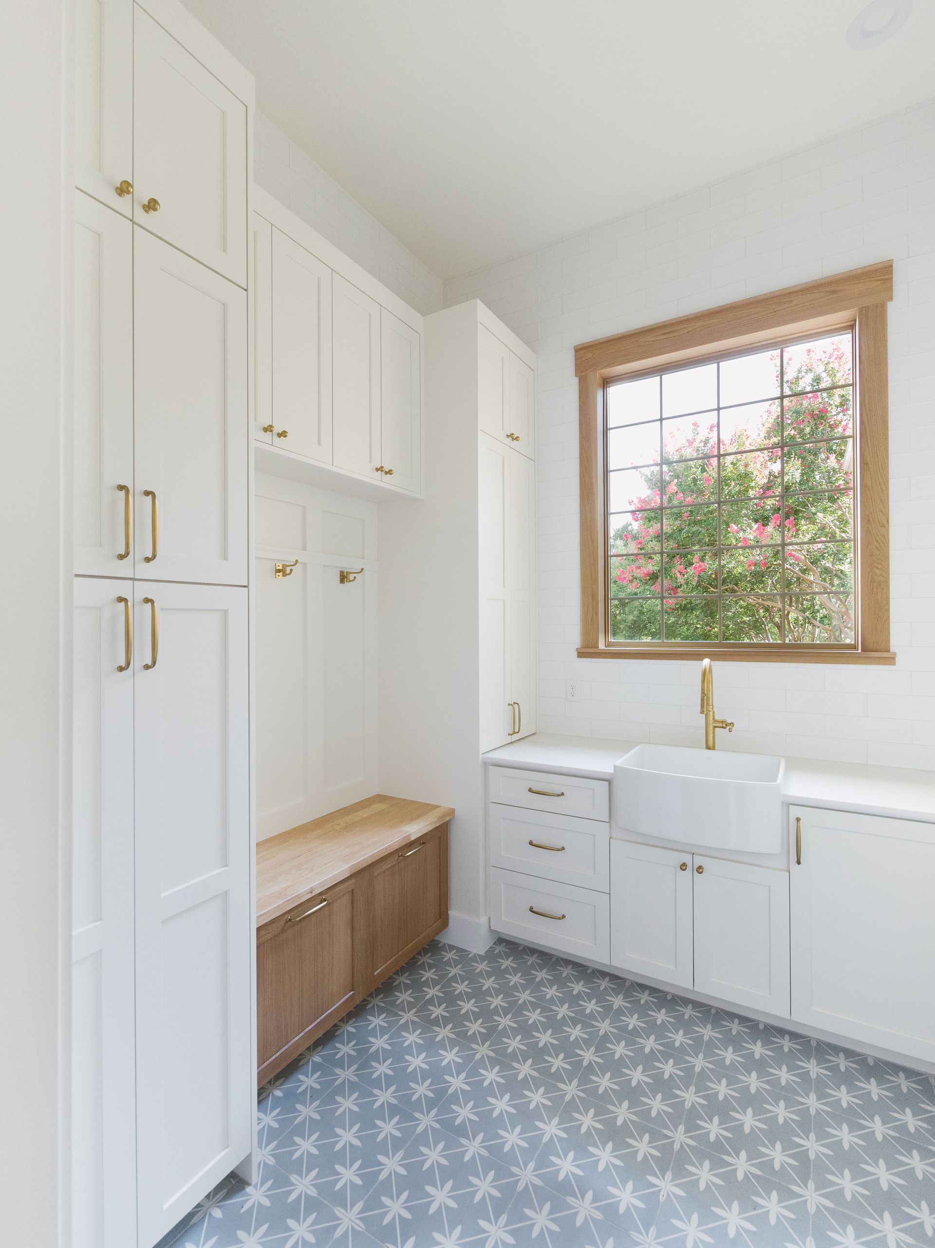 Laundry room with white cabinets, wooden bench, patterned blue floor, and a window.