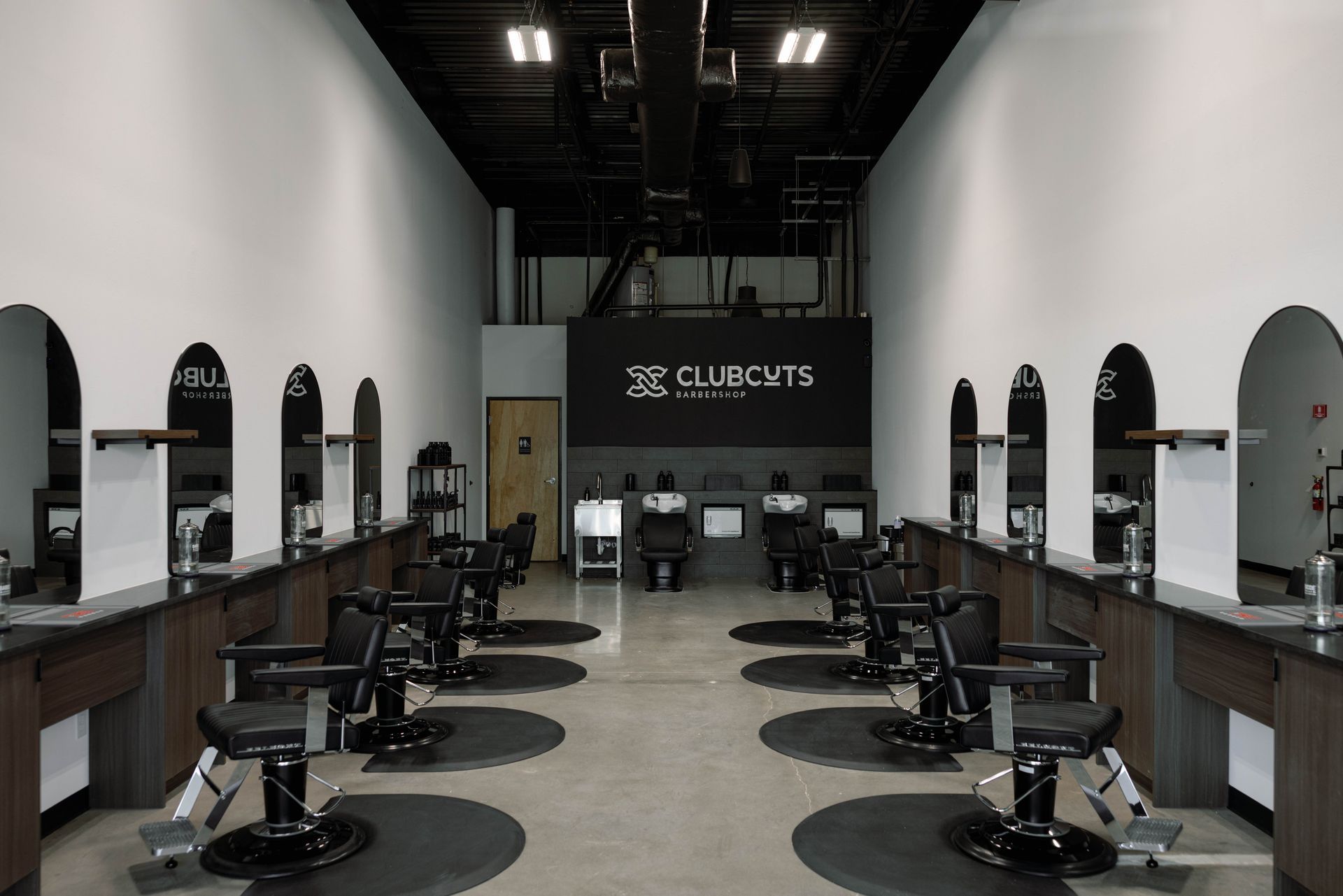 Interior of a barbershop with multiple styling chairs, mirrors, and the C. Cuts logo on the back wall.