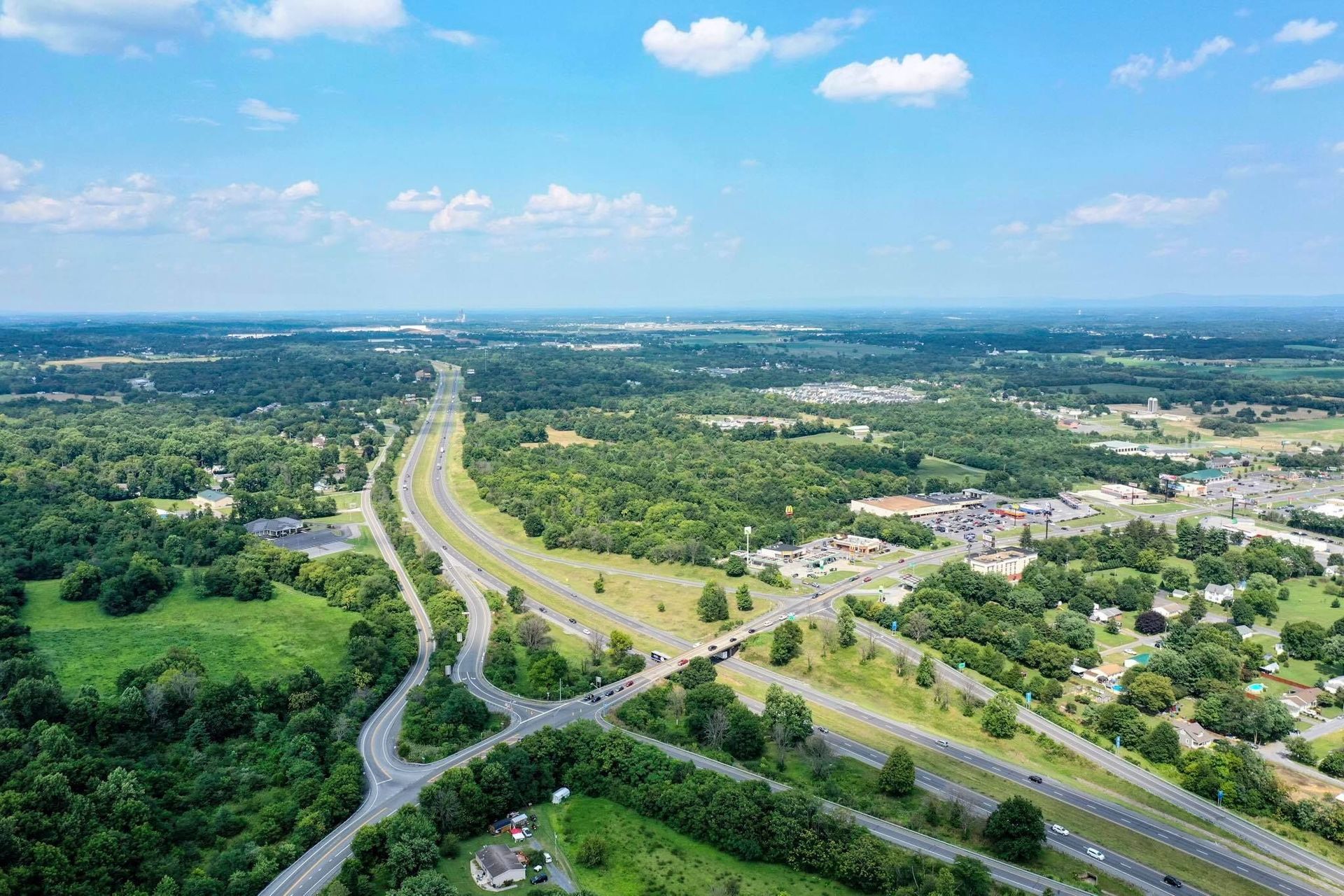 An aerial view of a highway surrounded by trees and fields on a sunny day. An aerial view of a highway surrounded by trees and fields on a sunny day.