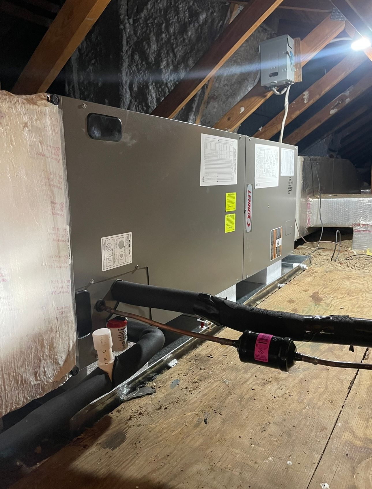 A row of air conditioners are sitting on top of a wooden floor in an attic.