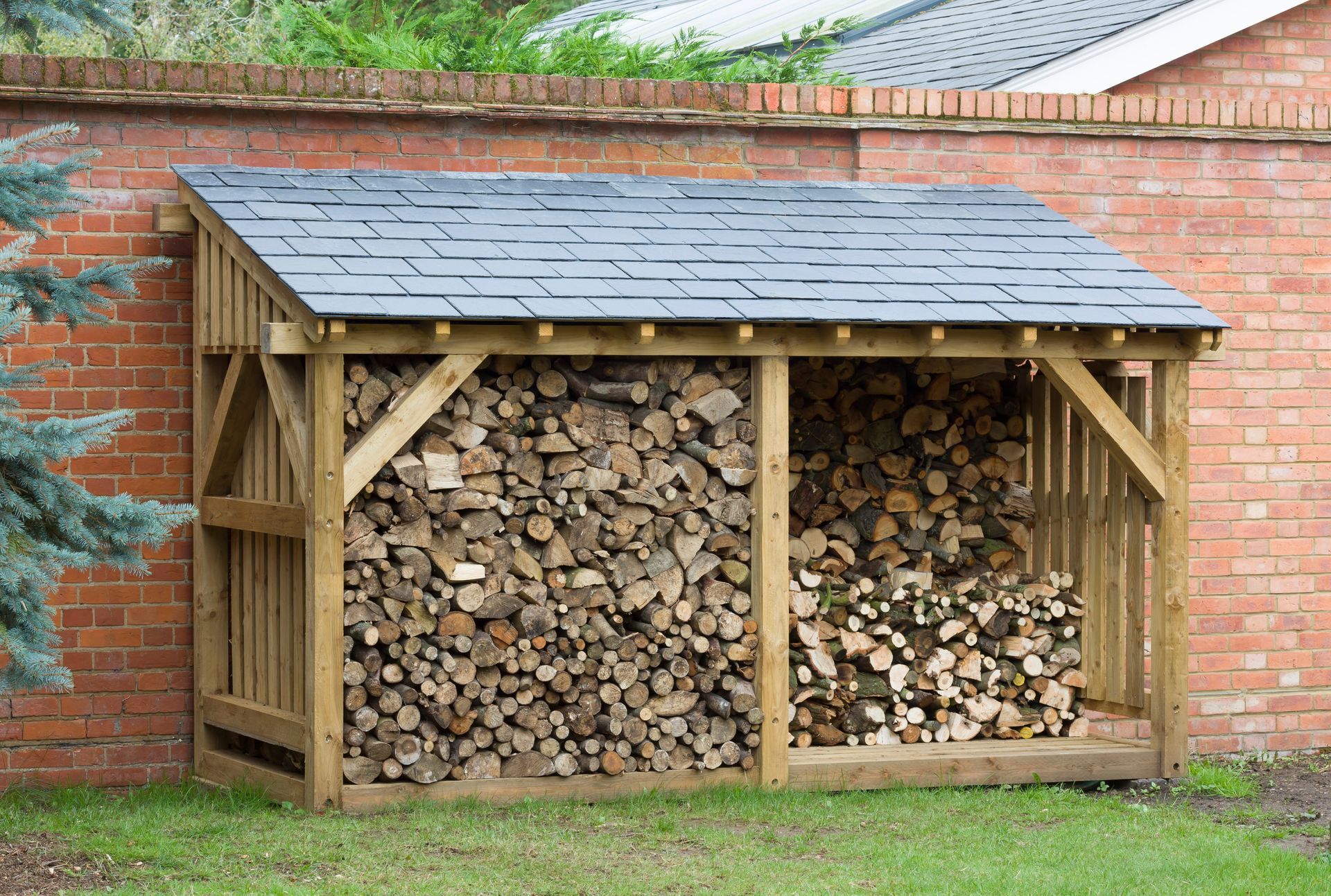 Wooden firewood storage shed against a red brick wall, filled with logs.