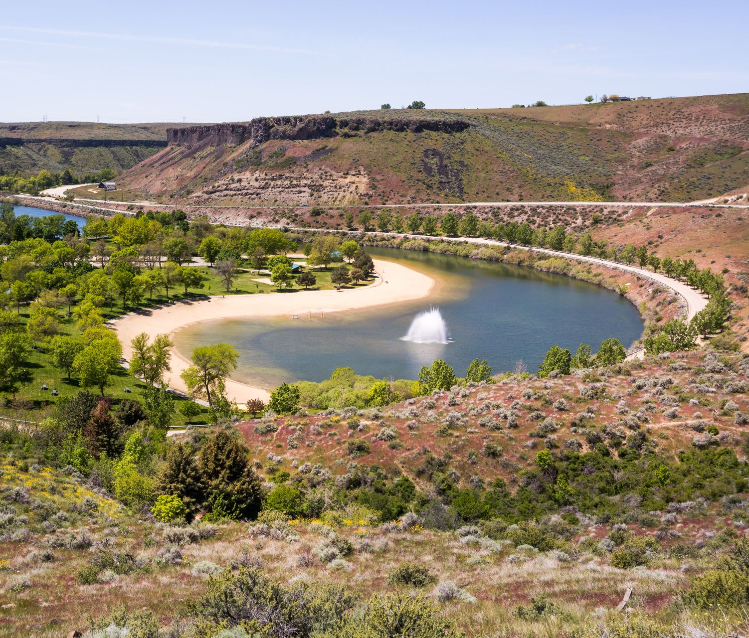 Person relaxing in a hot spring between large tan rock formations under a clear blue sky
