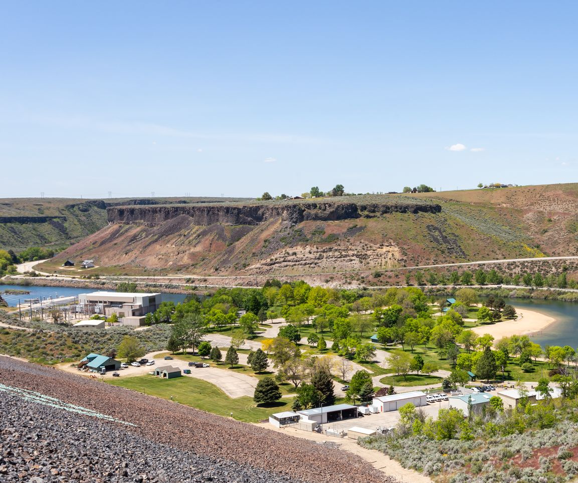 Wide rocky canyon with a river, green trees, and a small campground under a clear blue sky