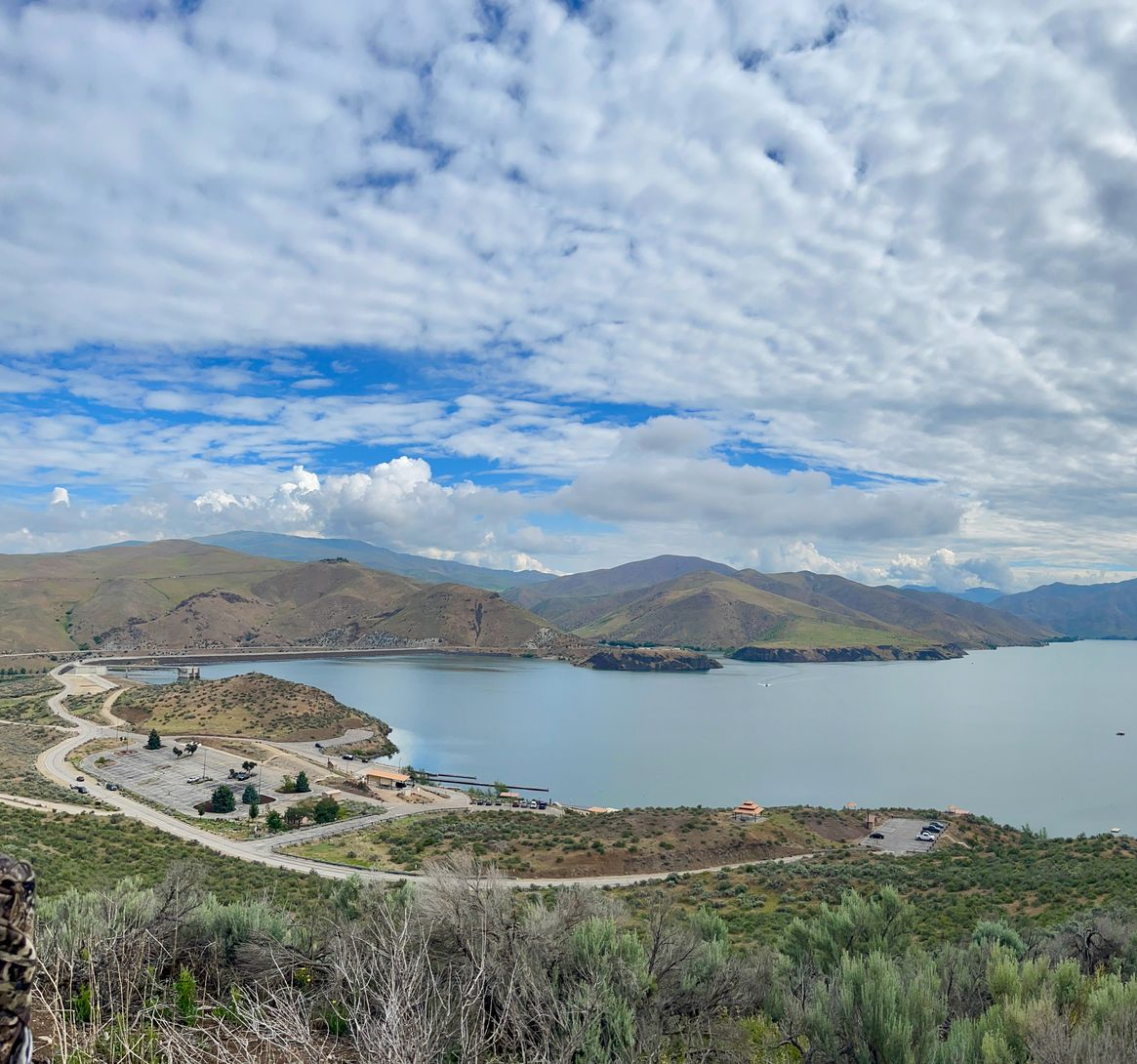 Wide bay with blue water, curving shoreline road, distant hills, and a cloudy sky