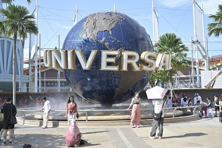 Universal Studios globe sign with people walking in front of it on a sunny day