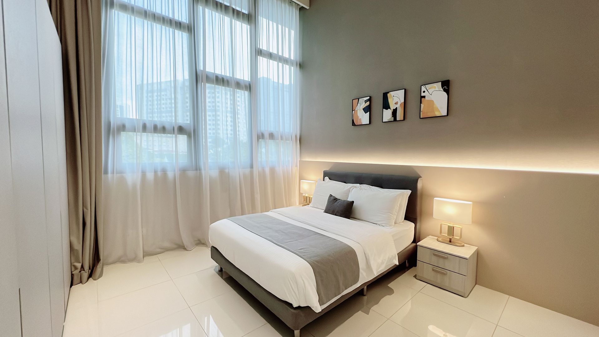 Bright modern bedroom with a bed, large window with curtains, bedside table, and wall art.