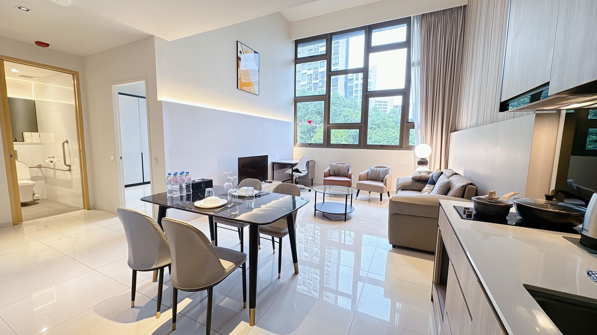 Modern living room with beige sofas, dining table, large windows, and a wall-mounted TV