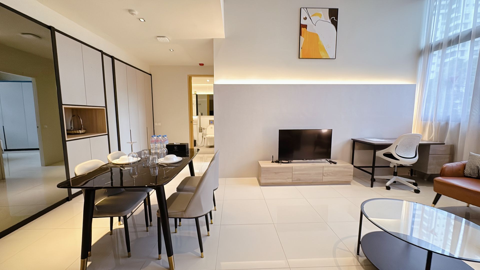 Modern open-plan living room and dining area with neutral decor, TV console, and large windows with sheer curtains