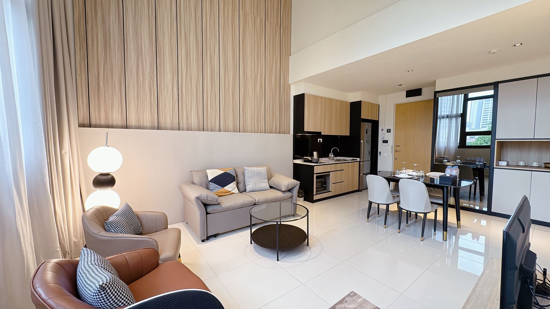 Modern open-plan living room and kitchen with gray sofa, round table, dining area, and wood slat accent wall