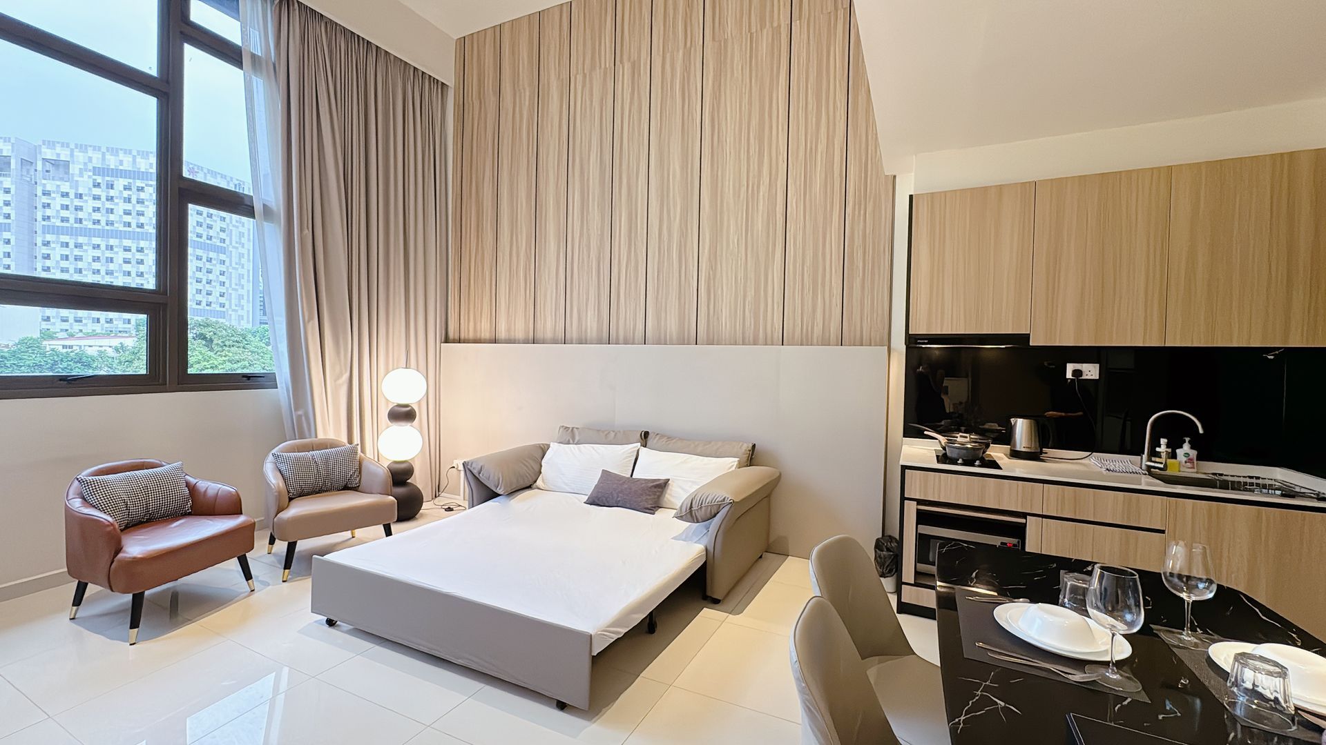 Modern hotel room with large bed, window seats, desk, and kitchenette