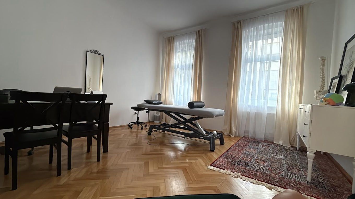 Bright living room with piano, massage table, windows, rug, and parquet floor