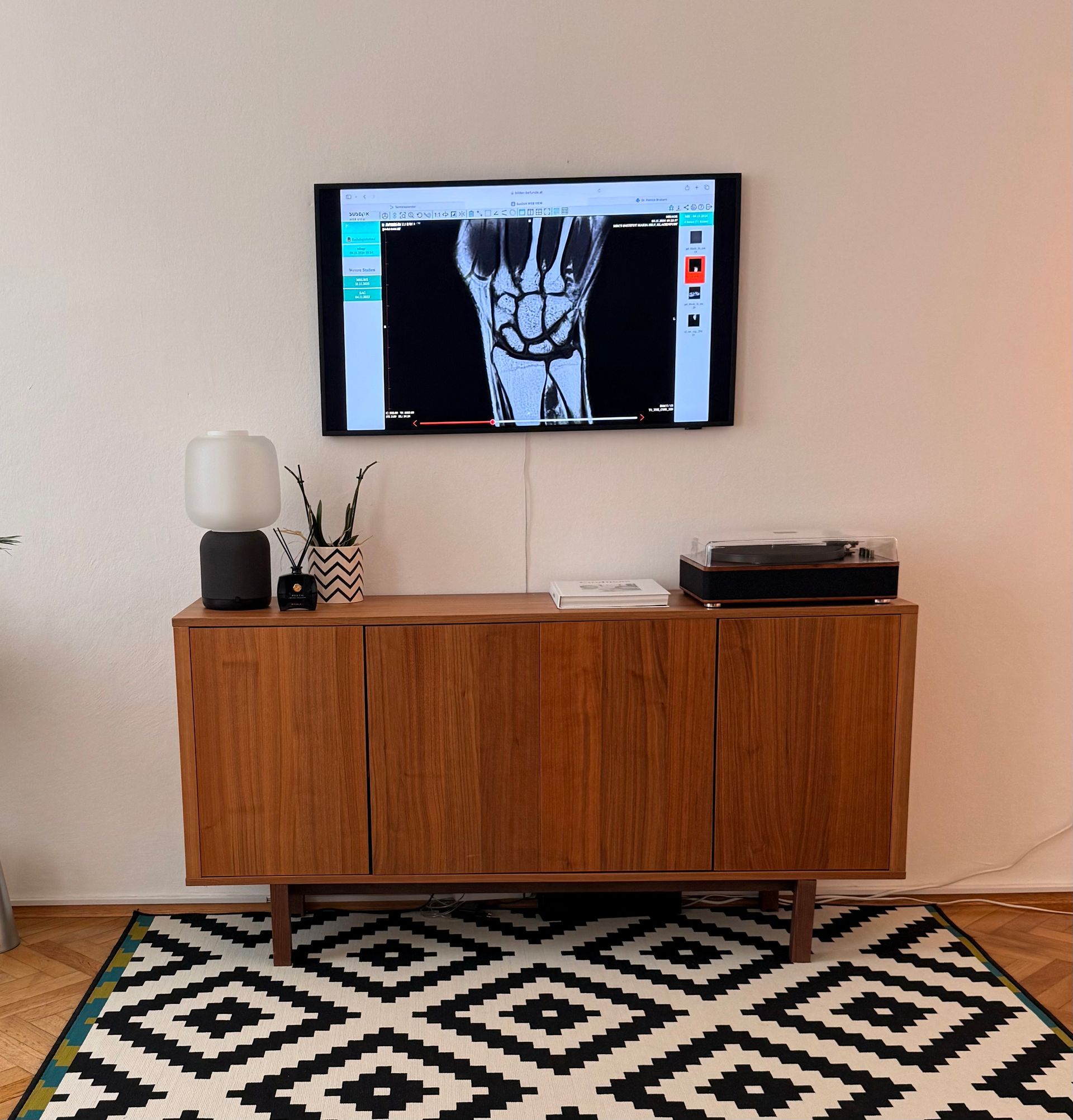 TV mounted above wooden cabinet in a minimalist living room with black-and-white rug