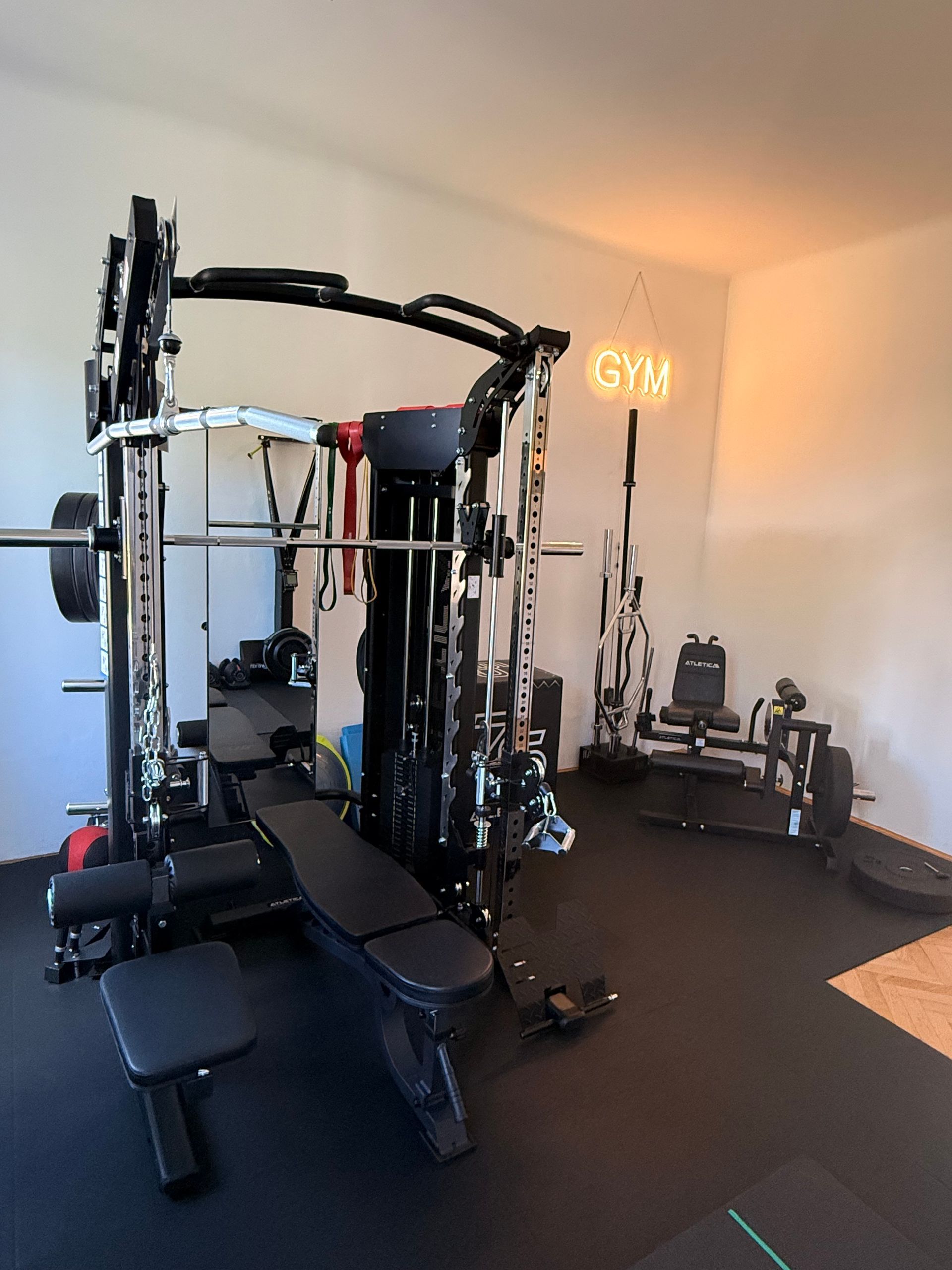 Home gym with weight machine, adjustable bench, mirrors, and dumbbells on black flooring.