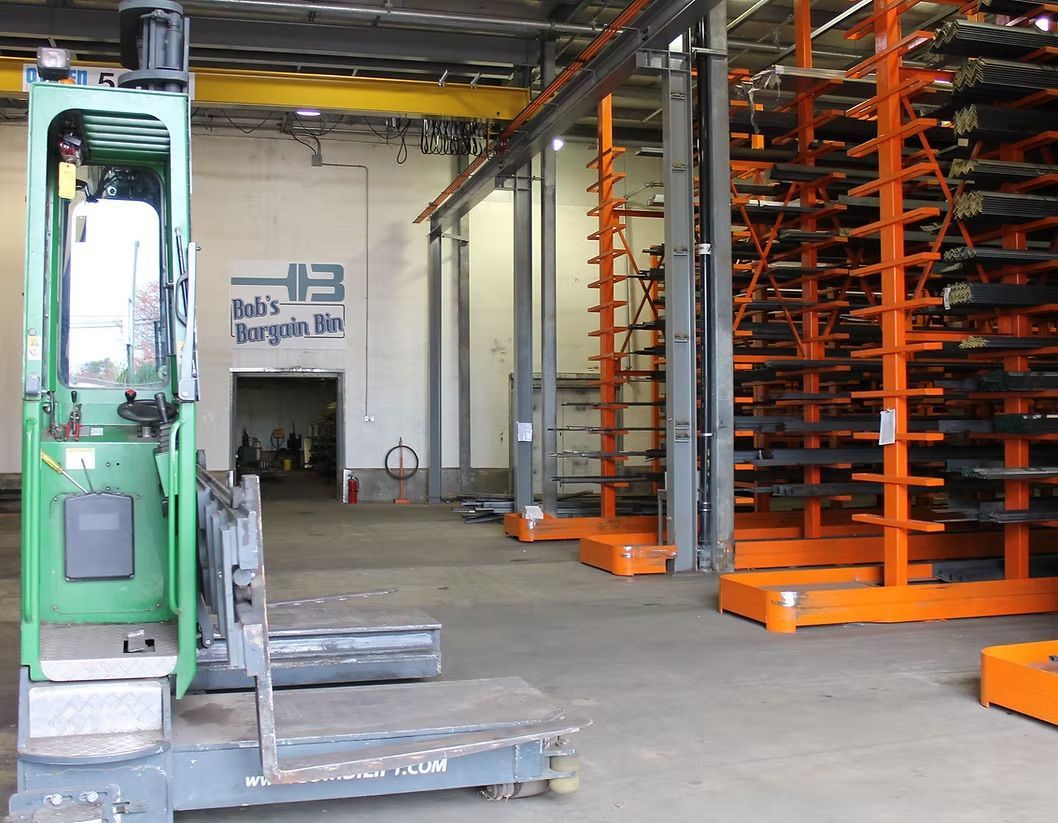 A green industrial forklift parked in a warehouse with orange storage racks holding metal materials.