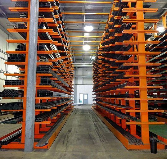 Two rows of orange cantilever industrial storage racks holding various metal materials in a warehouse.