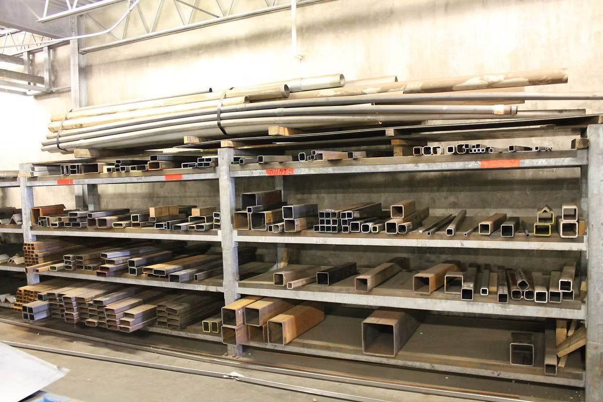 A metal rack containing various shapes and sizes of steel tubing and structural bars in a storage or workshop setting.