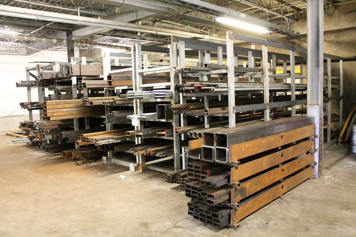 A warehouse storage rack filled with organized metal beams, pipes, and rectangular steel tubing.