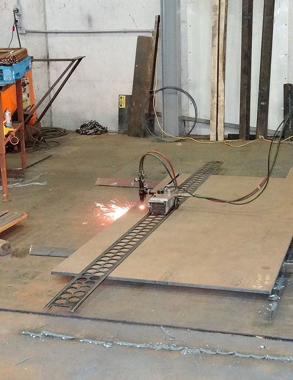 A track-mounted plasma cutter slices through a large metal sheet in a workshop, producing bright orange sparks.