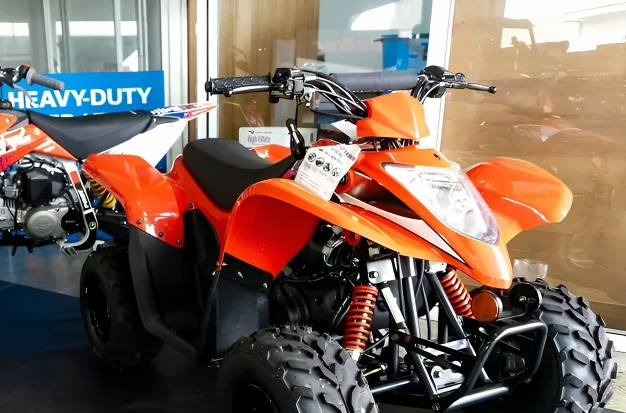 An Orange ATV Is Parked In Front Of A Sign That Says Heavy Duty — Coastal Farm & Motorcycles In Babinda, QLD