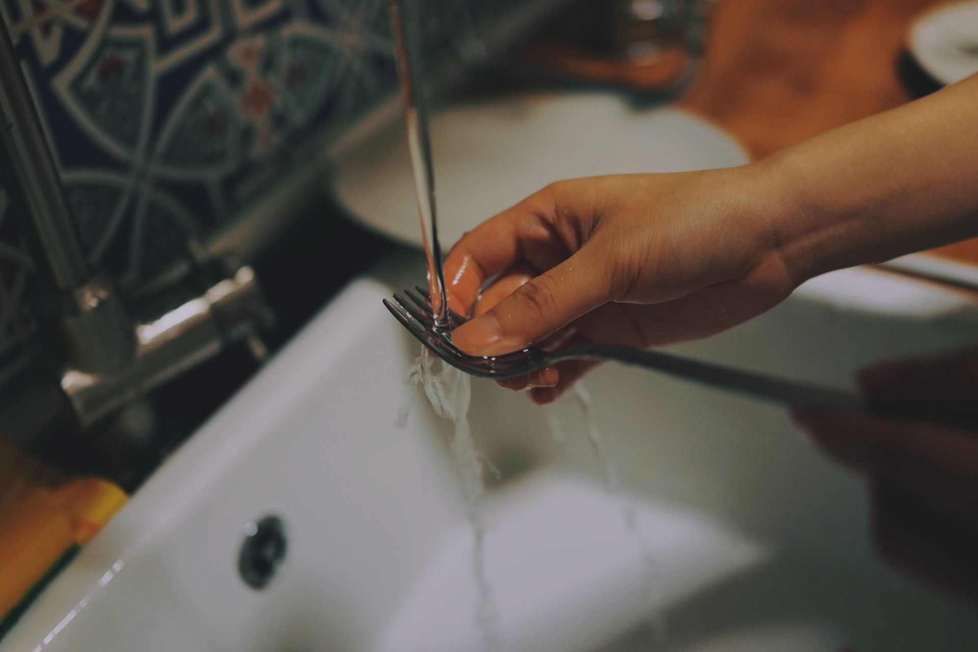 Hand rinsing a small metal object under running water in a white sink