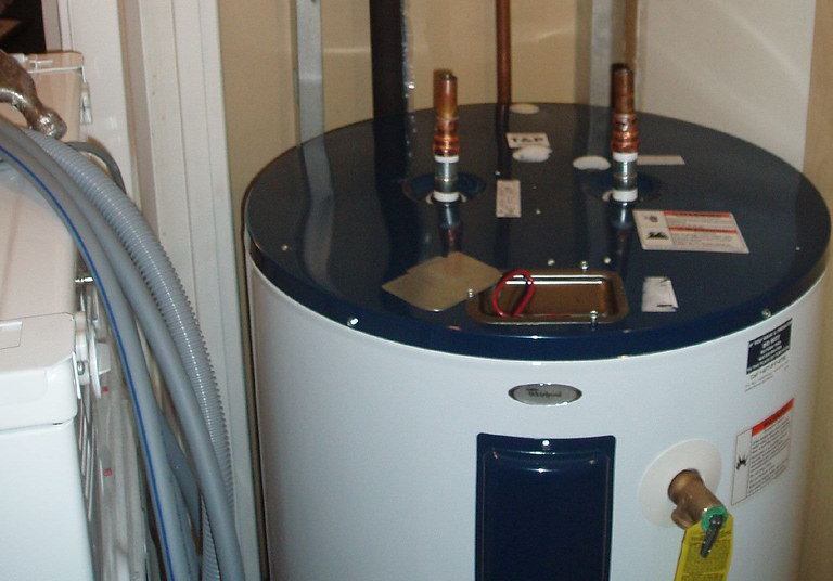 White water heater with dark top, pipes and valves, in a utility room