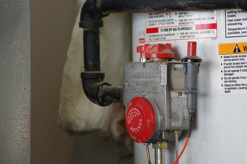 Water heater with gas control valve, black pipe, and labels on the tank side.
