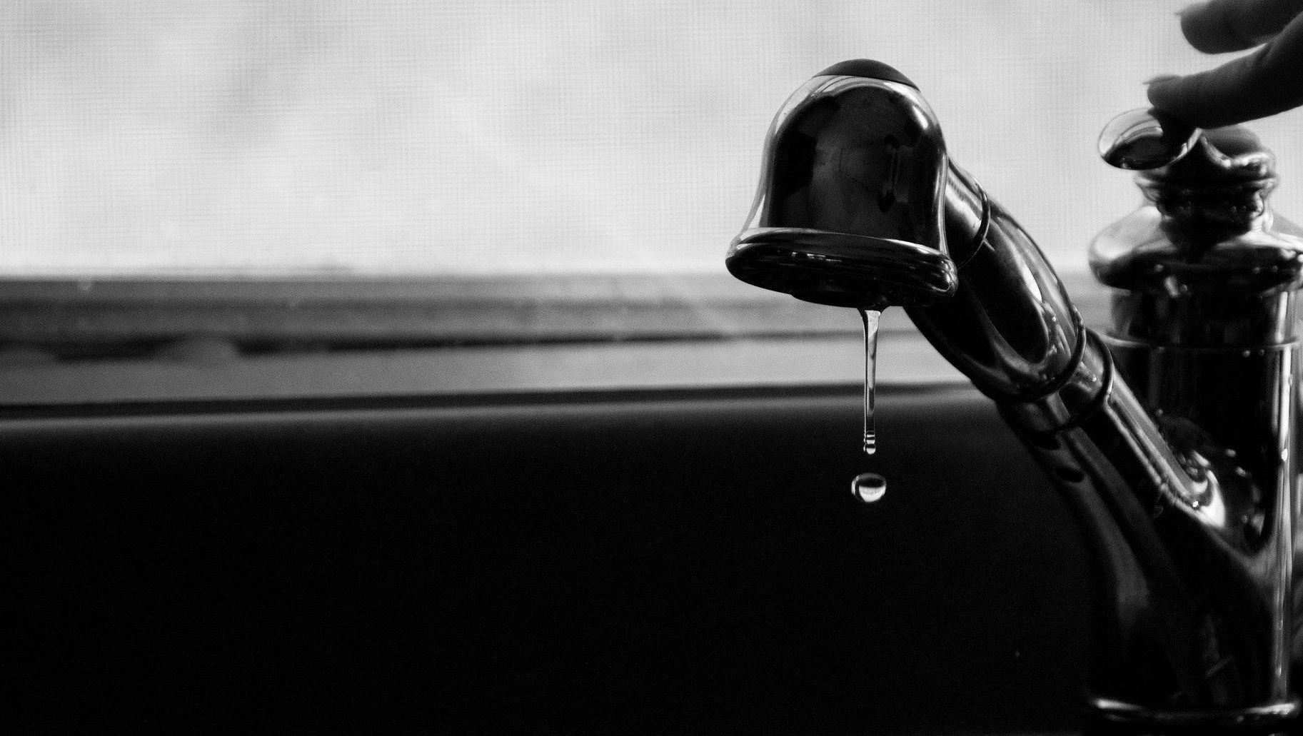 Black-and-white close-up of a dripping faucet over a sink.