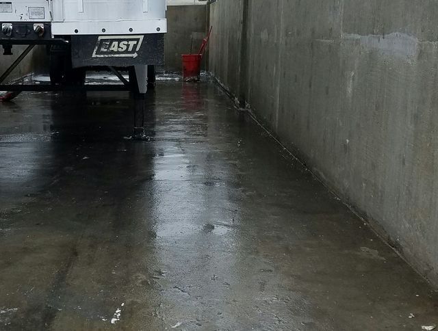 Wet concrete alley beside a parked truck, with rain reflections on the ground.