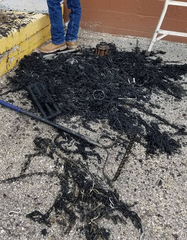 Black charred debris and melted material on gravel beside a yellow step and a person’s legs.